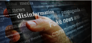 A hand holding a phone with words overlaid onto the image, such as ""disinformation", "fake news", and "propaganda"
